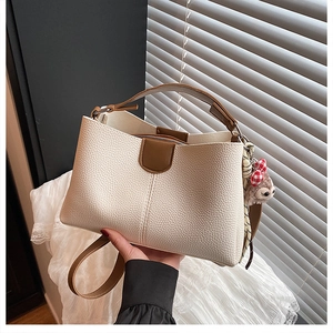 Detail of beige lychee texture PU leather tote with brown trim and plush charm
