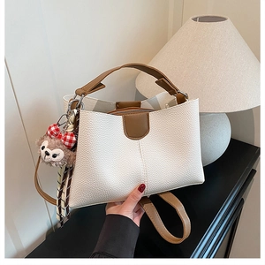 Detail view of white lychee leather tote with brown handles and plush koala charm