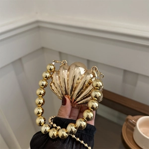 Elegant gold shell shaped crossbody bag with chunky pearl handle in a lifestyle setting
