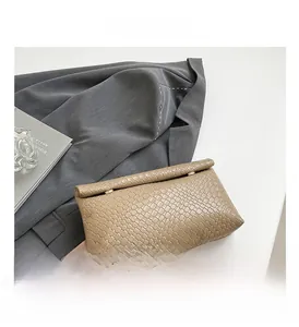 Detail of khaki woven clutch bag featuring intricate faux leather square texture and metal clasp