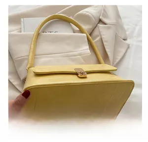 Détail de la texture cuir crocodile jaune et boucle en métal doré sur le sac baguette chic