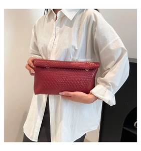 Detail of burgundy woven crossbody pillow bag held by model in white oversized shirt
