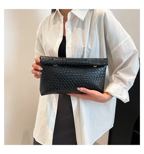 Détail d'une pochette enveloppe noire à texture tressée et anneaux métalliques dorés