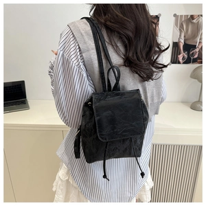 Détail du sac à dos noir texturé avec cordon de serrage et rabat porté par le mannequin