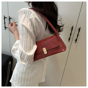 Détail du sac sous le bras rouge foncé à motif croco et fermoir doré porté