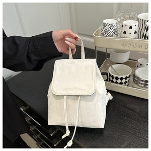 Detailed close-up of a white pleated mini backpack with drawstring and flap closure