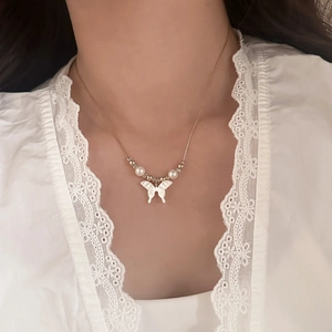 Detail of shell butterfly pendant necklace with pearls on a model wearing white lace