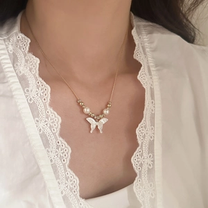 Elegant gold butterfly pendant necklace with white shell texture and pearls on female model