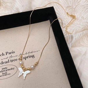 Macro detail of golden butterfly necklace with shell pendant and pearl accents