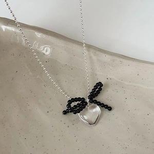 Detailed shot of transparent heart pendant with black beaded bow on silver chain