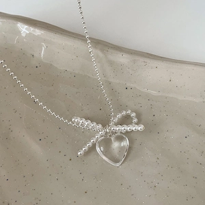 Detail of beaded bow and transparent heart pendant on a silver ball chain necklace