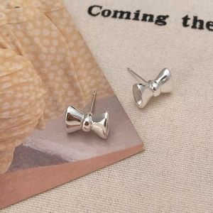 Détail de boucles d'oreilles nœud argentées sur un fond de toile crème minimaliste