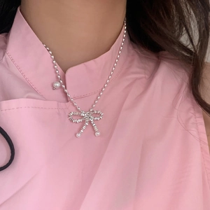 Silver bow pendant necklace with pearl accents on a metallic bead chain worn by a model