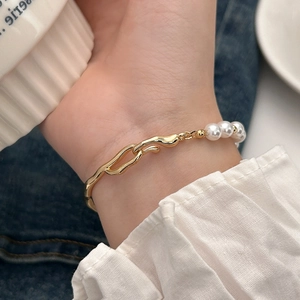 Detail of textured gold links and elegant pearls on wrist with soft fabric background