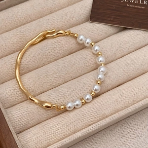 Detail of pearl and textured gold bracelet displayed on a beige jewelry display tray