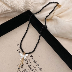 Détail du collier de perles en spinelle noire avec pendentif papillon blanc élégant