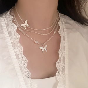 Detail of layered necklace with clear beads, faux pearls and white butterfly pendant
