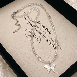 Detailed shot of clear beaded necklace with a white butterfly pendant on a canvas tray