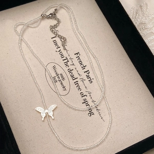 Close-up of double-layer beaded necklace with elegant white butterfly pendant in a jewelry box