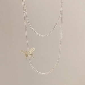 Minimalist transparent beaded necklace with a silver butterfly pendant on a beige surface
