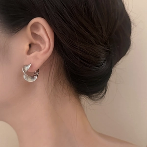 Boucles d'oreilles créoles torsadées argentées portées pour un look moderne et minimaliste
