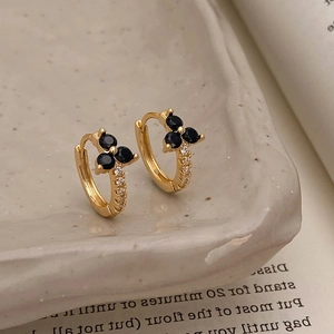 Detail of gold huggie earrings with black flower gems and white zircon on ceramic plate