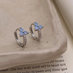 Close-up of silver hoop earrings featuring blue opal flowers and micro-set diamonds