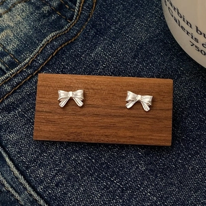 Detailansicht der silbernen Schleifen-Ohrstecker auf dunklem Holz und Denim-Stoff