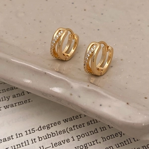 Détail de boucles d'oreilles doubles dorées avec zircons sur plateau céramique