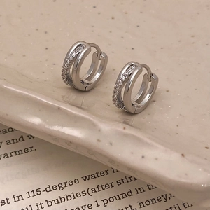 Détail de boucles d'oreilles doubles cercles argentées serties de zircons sur plateau
