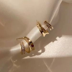 Macro shot of gold-plated double C-shape earrings with cubic zirconia on white silk