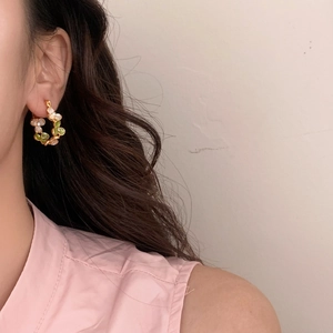 Gros plan de boucles d'oreilles florales en C en métal doré avec pétales verts