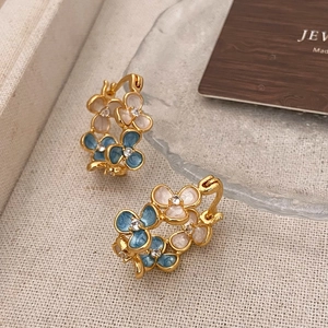 Gros plan de boucles d'oreilles fleurs dorées avec émail bleu et blanc et petit cristal