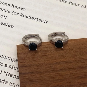 Detail of silver hoop earrings with a four-prong set round black zircon on a book background