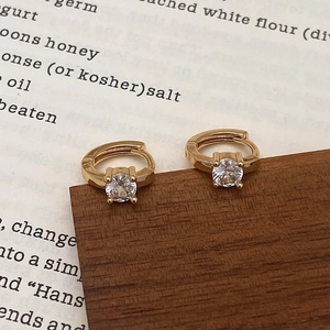 Macro detail of gold hoop earrings with sparkling round zircon on wooden display