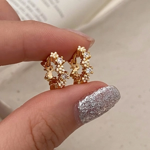 Nahaufnahme kleiner goldener Creolen mit weißen Blumen und funkelnden Kristallsteinen