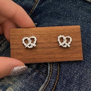 Dettaglio di orecchini a nodo d'argento con pavé di zirconi su sfondo di denim