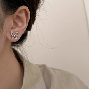Close-up of a silver hollow butterfly stud earring with sparkling cubic zirconia on model