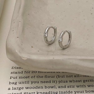 Detailed view of silver hoop earrings with square zircon on textured ceramic tray