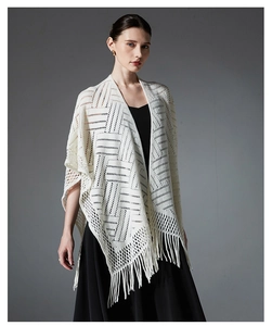 Détail du motif en tricot géométrique et longues franges sur un châle de couleur crème