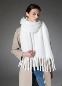 Close-up of white chunky knit scarf with thick braided tassels and fluffy yarn texture