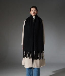 Detail of long black chunky scarf with thick fringe tassels styled on a wool coat
