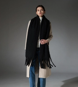Detailed view of black fuzzy mohair scarf with thick tassels styled with winter coat
