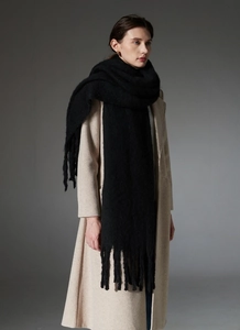 Close-up of a thick black knit scarf with long fringe details on a model in a beige coat