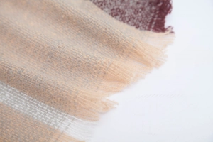 Gros plan d'une écharpe à carreaux beige et bordeaux montrant la texture et les franges