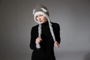 Detail of winter knit hat with white faux fur trim and long braided pompom tassels