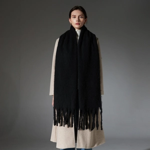 Thick black faux mohair scarf with chunky fringe tassels worn over a beige coat