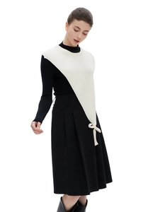 Detail of white asymmetric knitted shawl with bow tie paired with black pleated midi skirt