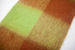 Macro detail of thick plaid scarf featuring soft brushed texture in green and orange