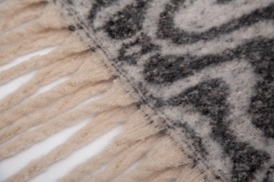 Macro detail of scarf showing textured bouclé yarn weave and fringe tassels
